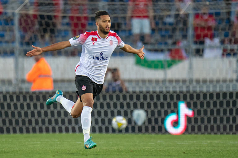 A bearded young man in football gear runs, arms out at his sides and fingers stretched.