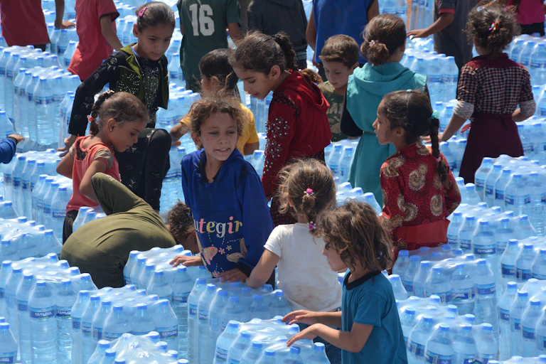 Children stand between rows of packaged bottles of water.
