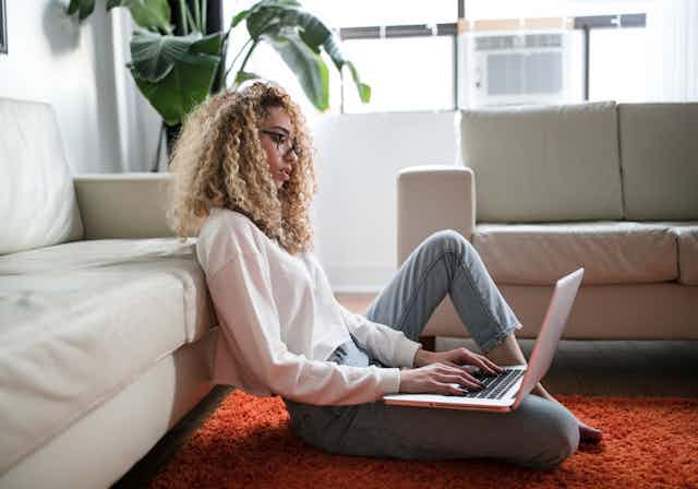 Woman sits on her living room floor, researching on her laptop.