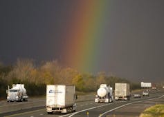 A rainbow is seen descending over a highway as transport trucks drive along it.