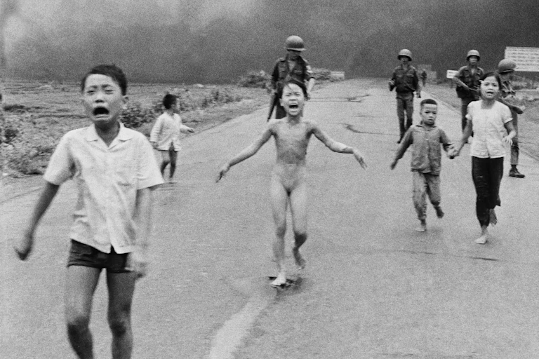 Frightened and tearful children, including one without clothes, run down a road in front of soldiers.