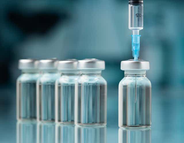 syringe inserted in first of a row of vaccine vials