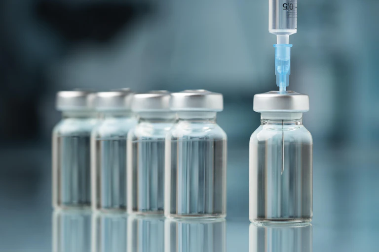 syringe inserted in first of a row of vaccine vials