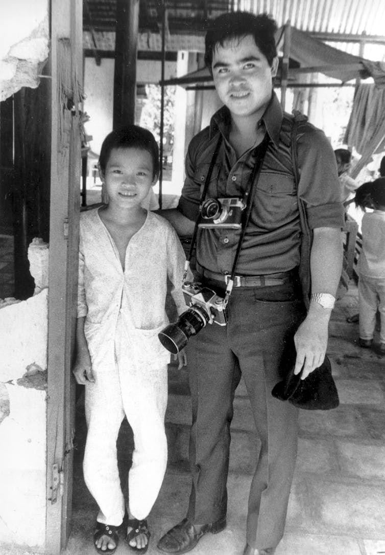 a young girl stands next to a man who has a camera slung from his neck. Both are smiling.