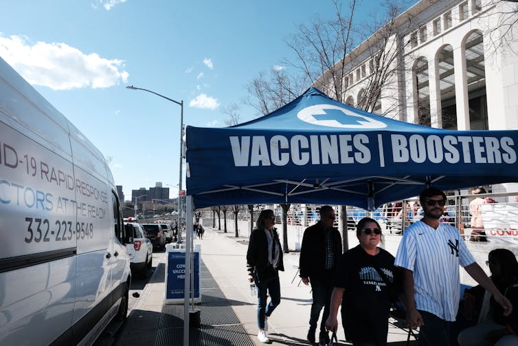 people walk near a tent marked 'Vaccines | Boosters'
