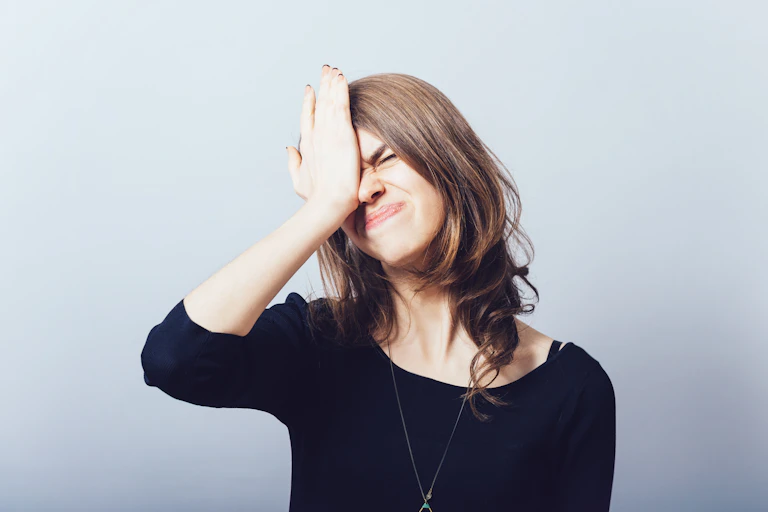 Dark haired woman palms her face with a frustrated expression