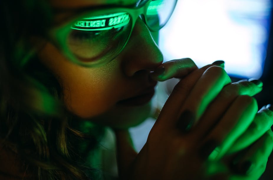 Woman wearing glasses washed in green light reads from a screen.