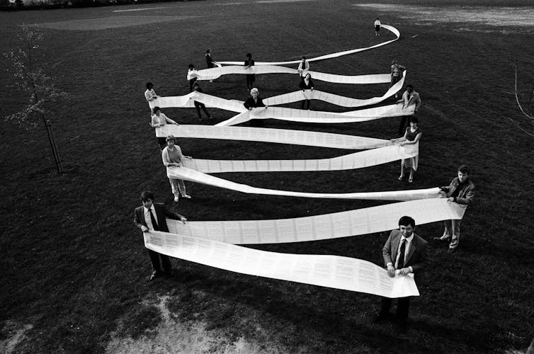 A black and white shot of people standing in a field holding a very long piece of paper.