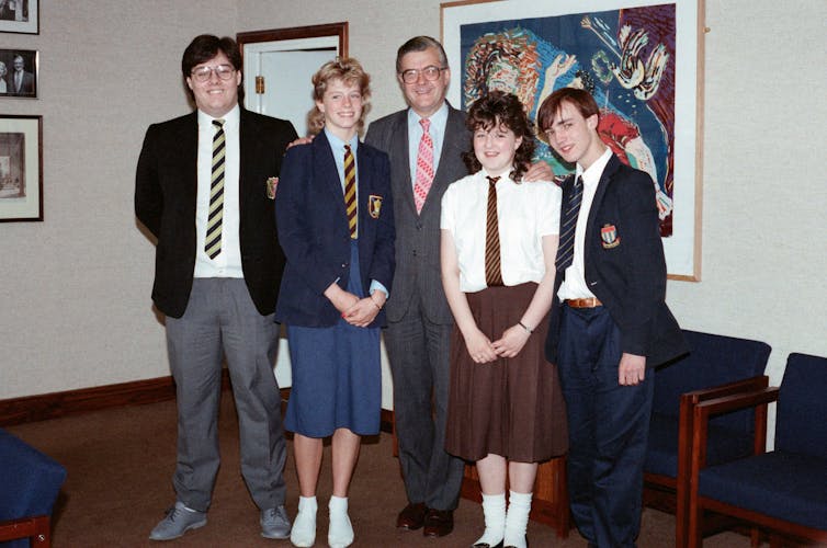 Teenagers in uniform pose for an indoor group photograph with a man in a suit.