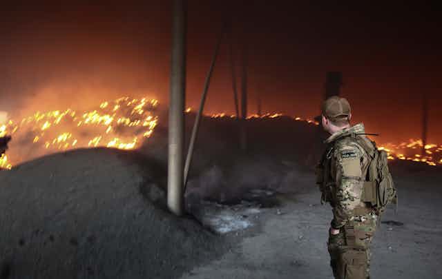 A Ukrainian soldier looks on  at a sunflower seeds storage on fire after shelling on a farm close to the front line near the city of Bakhmut, Donetsk region,