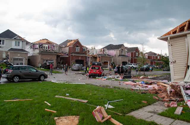 Ground-level view of a neighbourhood that has been struck by a tornado: roofs missing, insulation and wood strewn across the ground.