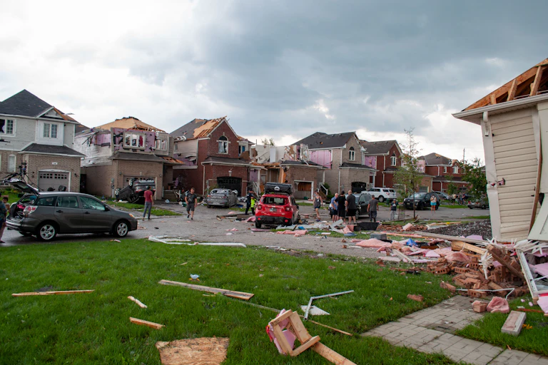 Ground-level view of a neighbourhood that has been struck by a tornado: roofs missing, insulation and wood strewn across the ground.