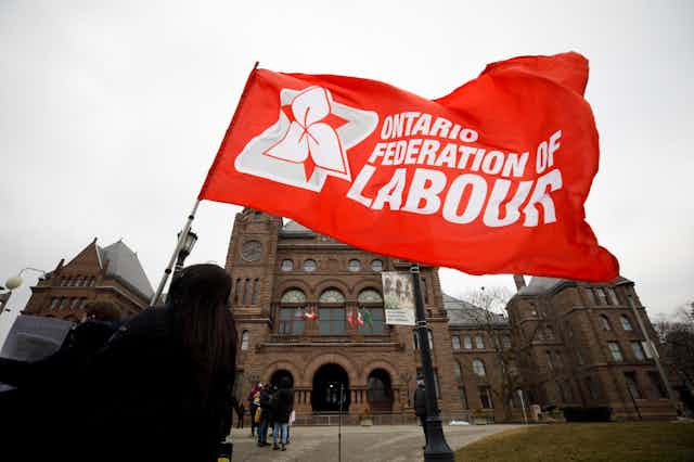 Someone carries a red flag that says 'Ontario Federation of Labour'
