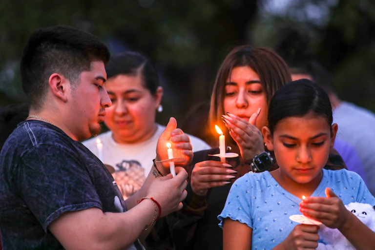 A group of people shield the flames of candles.