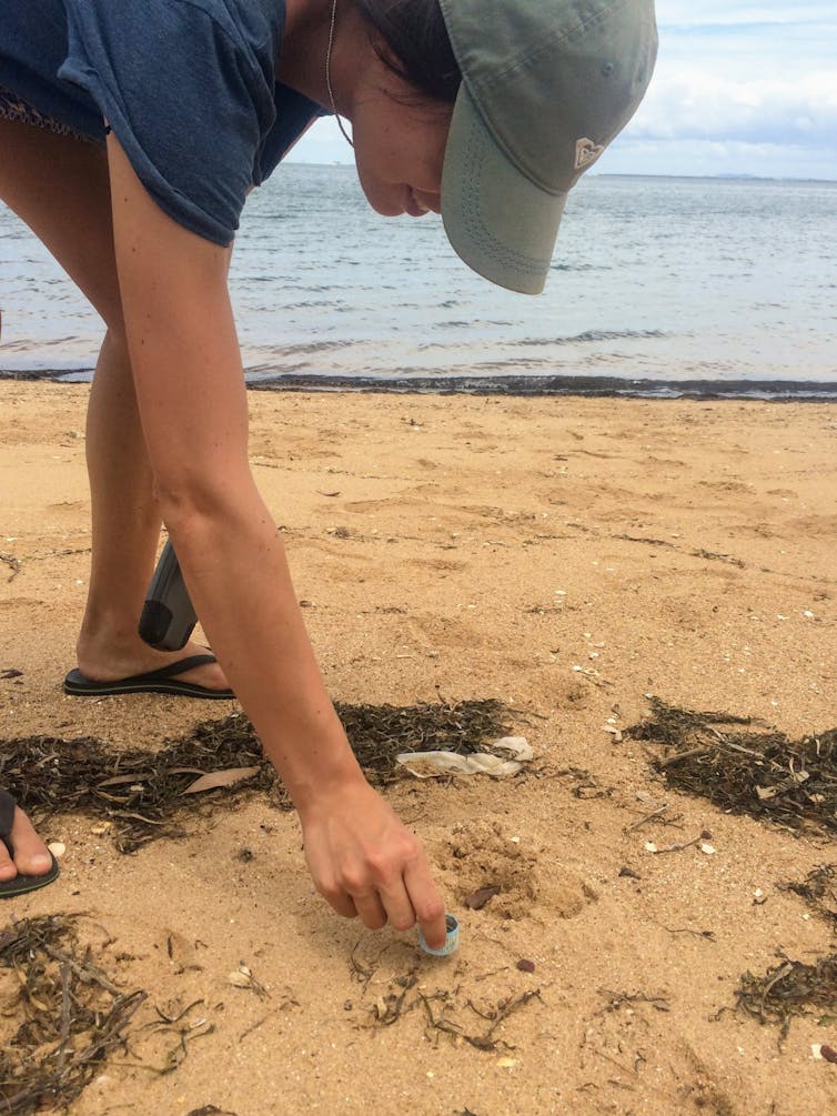 Woman picking up a litter bottle cap on the beach