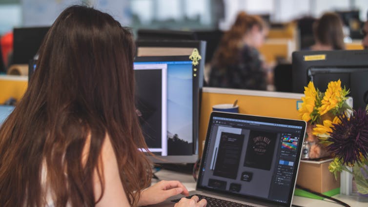 Woman with long brown hair types on a laptop at her desk.
