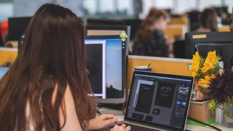 Woman with long brown hair types on a laptop at her desk.