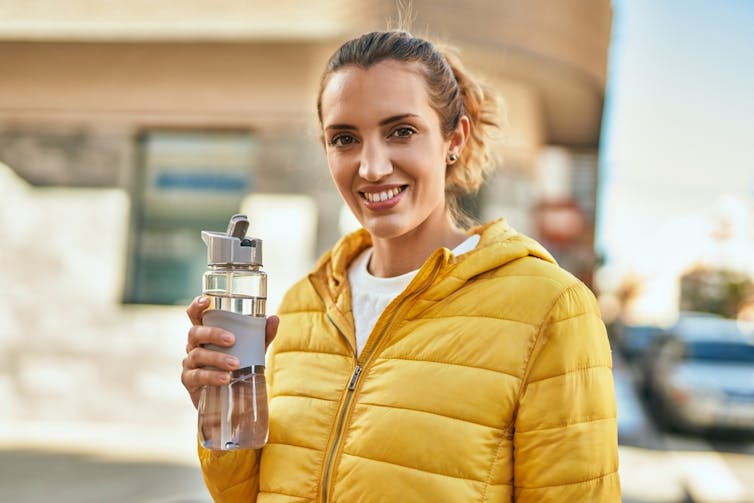 Smiling woman wearing yellow puffer jacket holding water bottle