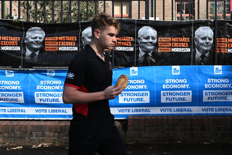 A young voter walks past election advertising at the polling booth.