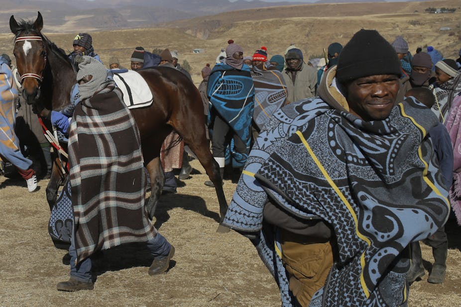 Men wearing blankets and hats lead a horse.