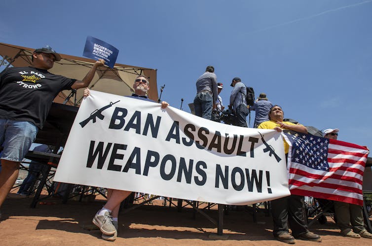 People hold a banner that says Ban Assault Weapons Now