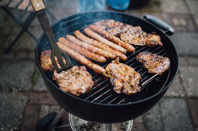 Many pieces of meat over a smoky round barbecue.