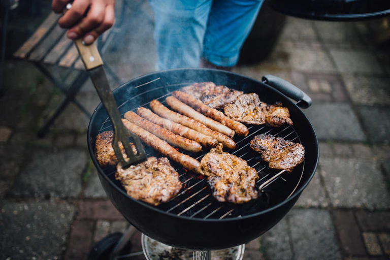 Many pieces of meat over a smoky round barbecue.