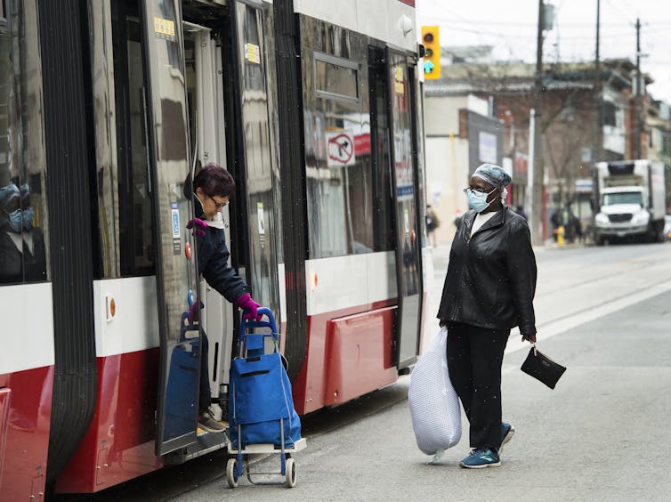 A woman wearing a mask waits to get into a streetcar as a passenger steps out.