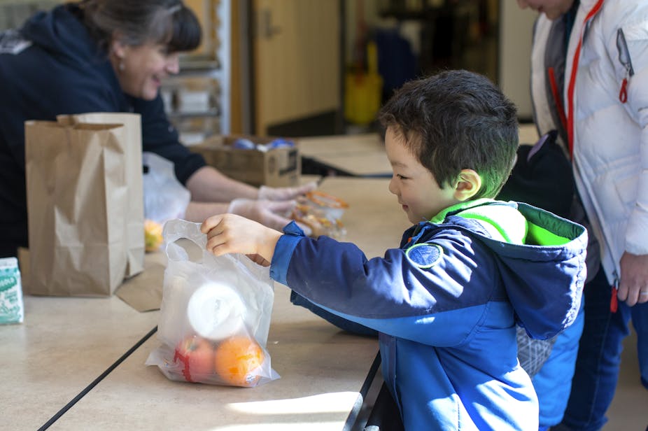 A young boy wearing a blue jacket picks up a bag of food from school