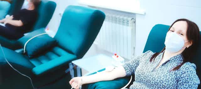 Women sitting in chair wearing mask donating blood