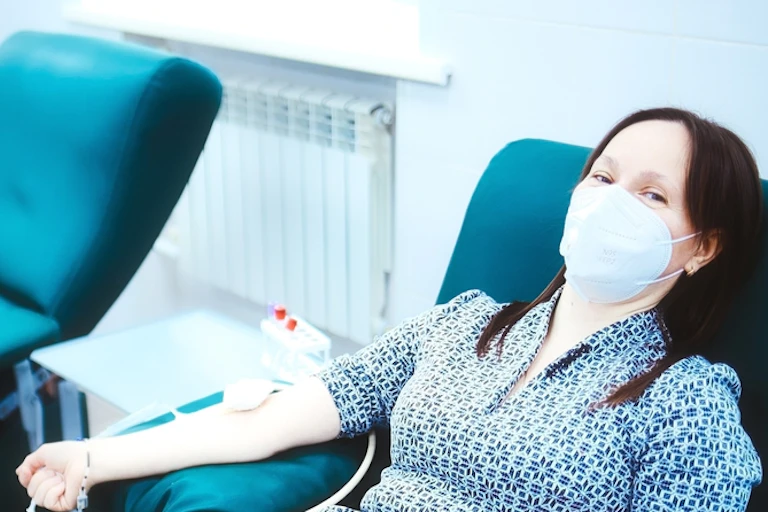 Women sitting in chair wearing mask donating blood