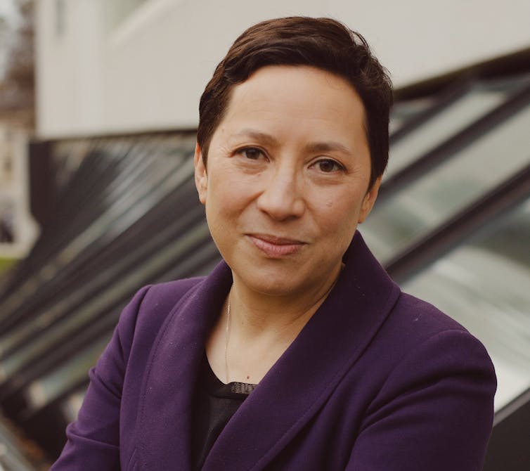 short-haired woman smiling at the camera, wearing a purple blazer