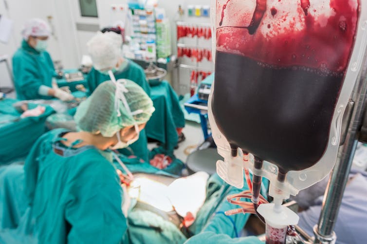 Blood bag hanging in operating theatre while surgeons operating
