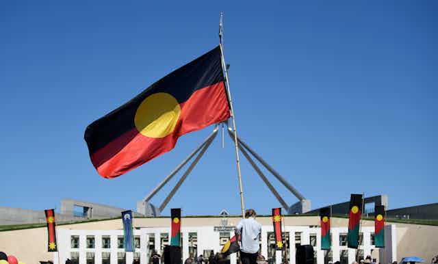 A person holds an Aboriginal flag in front of Parliament house.