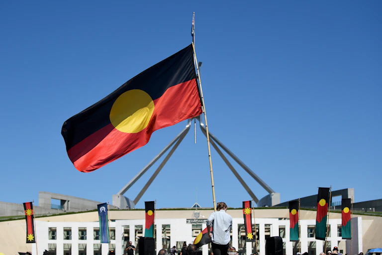 A person holds an Aboriginal flag in front of Parliament house.