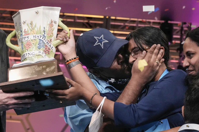 A spelling bee champion holds their trophy aloft while their parents congratulate them.