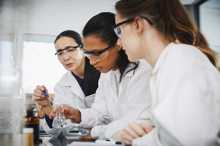 Female chemistry teacher explaining to young multi-ethnic students in laboratory