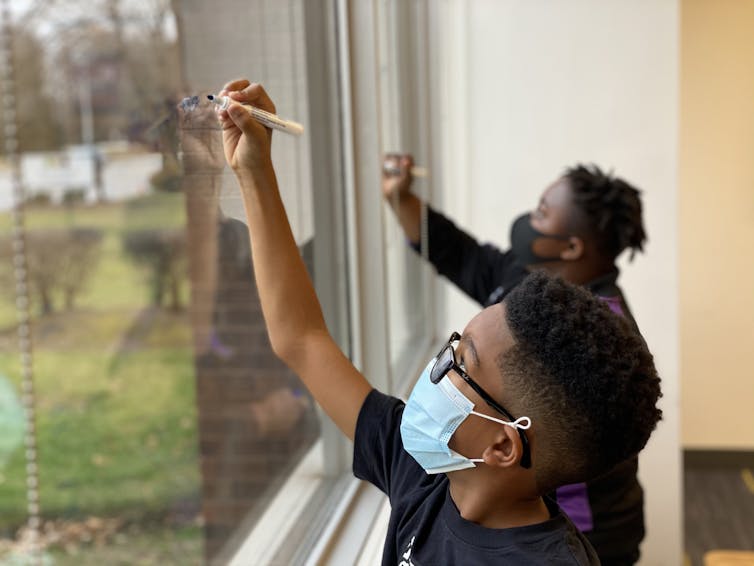 Students seen writing on a window with whiteboard markers.
