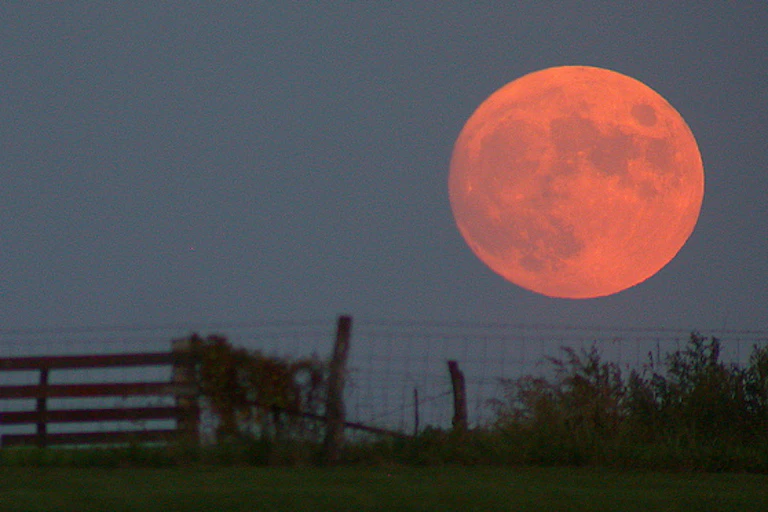 A huge red moon next to a fence.
