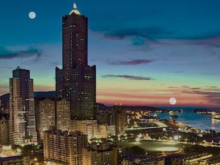 An image of a city skyline with two images of the Moon - one higher in the sky and one near a distant horizon.