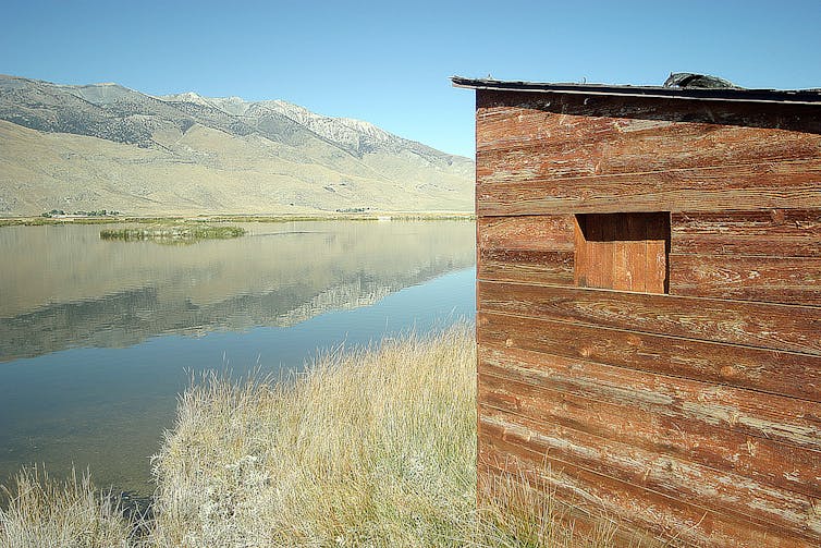 A wooden shed overlooks a wetland with mountains in the background.
