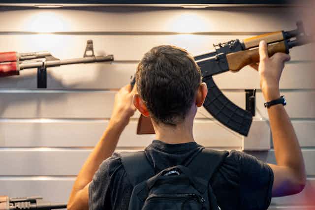 The back of a boy's head is seen in front of a wall of guns.