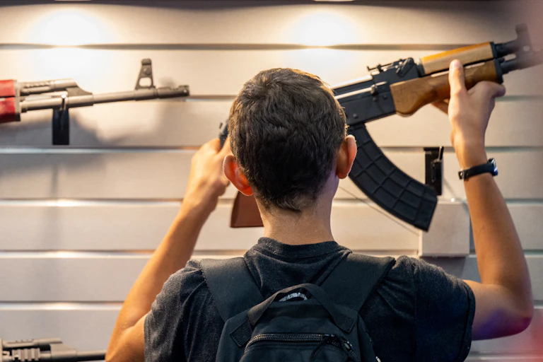 The back of a boy's head is seen in front of a wall of guns.