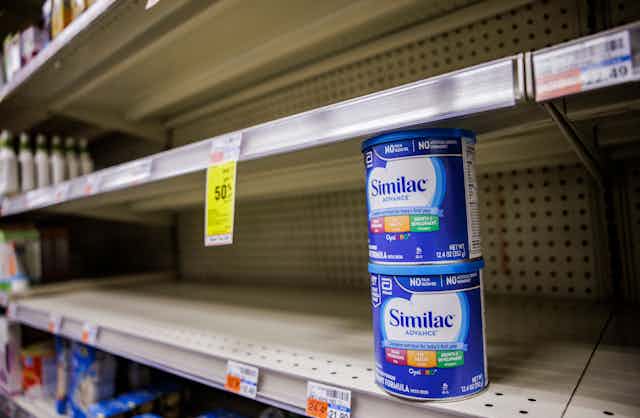 Two cans of Similac baby formula on otherwise empty grocery store shelves.
