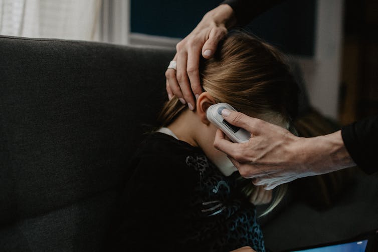 adult takes girl's temperature with ear thermometer