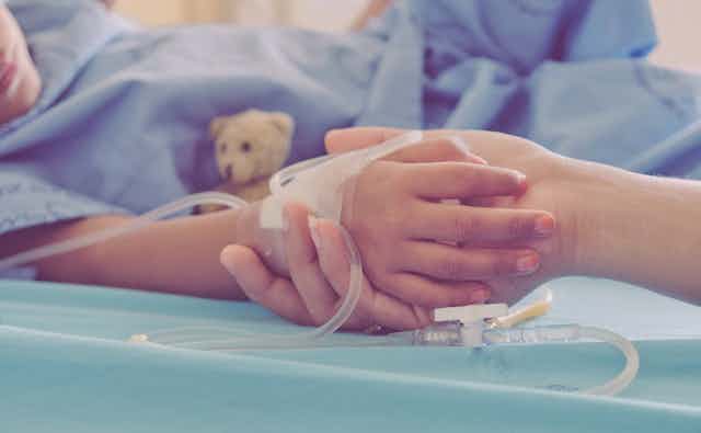 parent holds child's hand in hospital gown