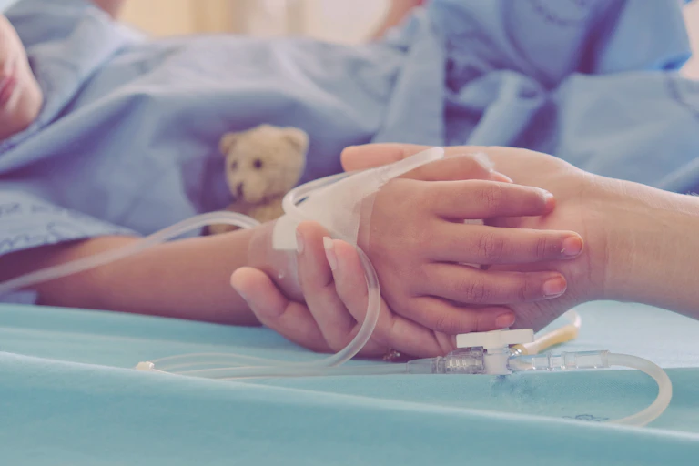 parent holds child's hand in hospital gown