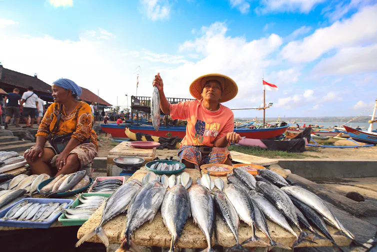 A fishmonger sits behind a platter of fish in a market