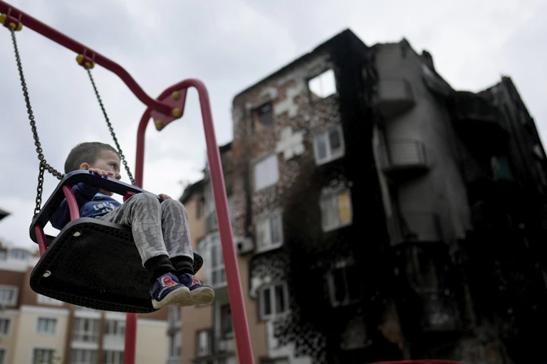 A boy sits in a swing outside a destroyed building.