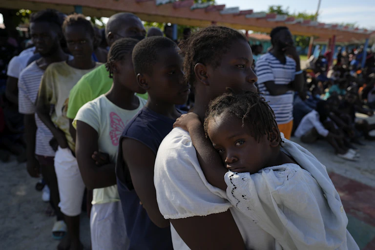 A girl in her mother's arms looks at the camera as they stand in a line.